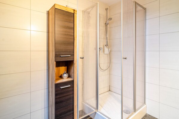 Un baño con ducha, un armario de madera y piso de baldosas.