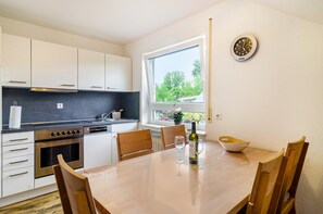 A modern kitchen with white cabinets, a built-in oven, and a dining area with a table and chairs.
