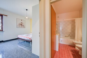 A hotel room with a bed, a bathroom with a bathtub and toilet, and a hallway leading to another room.