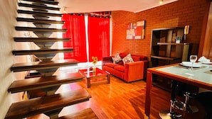 Una sala de estar moderna con una escalera de madera, cortinas rojas, un sofá rojo y una pared de ladrillo.