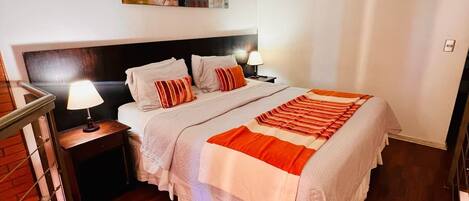 A bedroom with a large bed, a nightstand with a lamp, a headboard, and a painting on the wall.