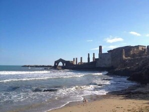 Une plage avec des vagues, une structure en pierre et un ciel dégagé.