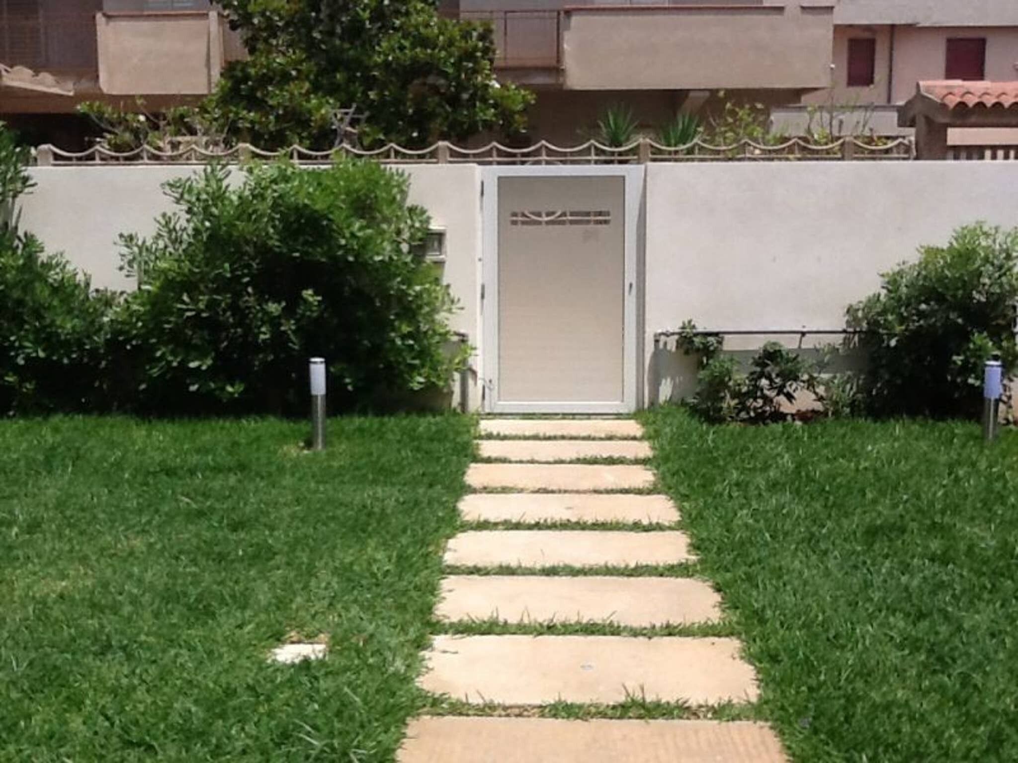 Un sentiero conduce a un edificio con una porta, immerso nel verde e delimitato da una recinzione.