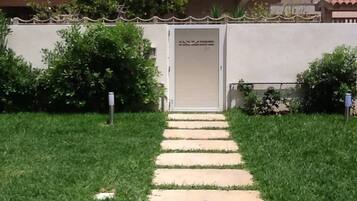 Un sentiero conduce a un edificio con una porta, immerso nel verde e delimitato da una recinzione.