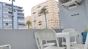 Ein Balkon mit weißen Kunststoffstühlen und einem Tisch, mit Blick auf eine Stadtlandschaft mit hohen Gebäuden und Palmen.