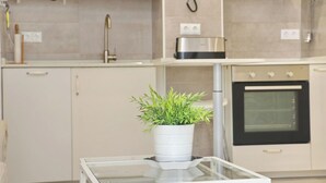 Eine moderne Küche mit Mikrowelle, Toaster und Backofen, einer Topfpflanze auf einem Glastisch und einem weißen Schrank.