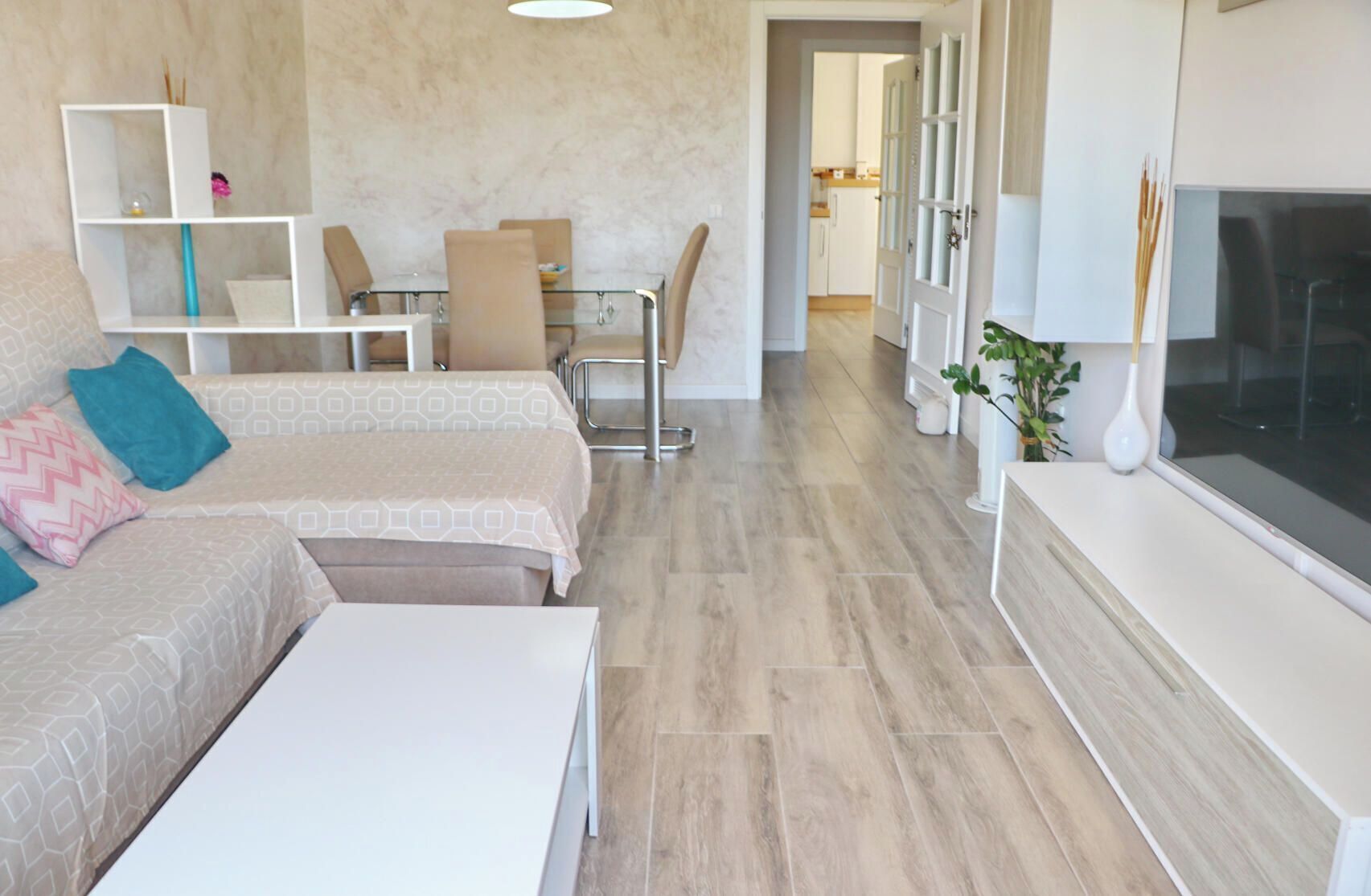 Een moderne woonkamer met een bank, een salontafel, een televisie en een eethoek met stoelen en een tafel.