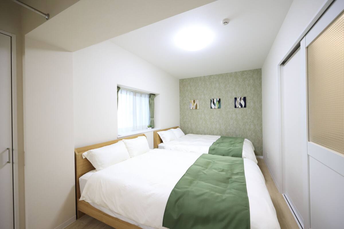 Une chambre d’hôtel avec deux lits, une fenêtre avec des rideaux et un mur orné de trois tableaux encadrés.