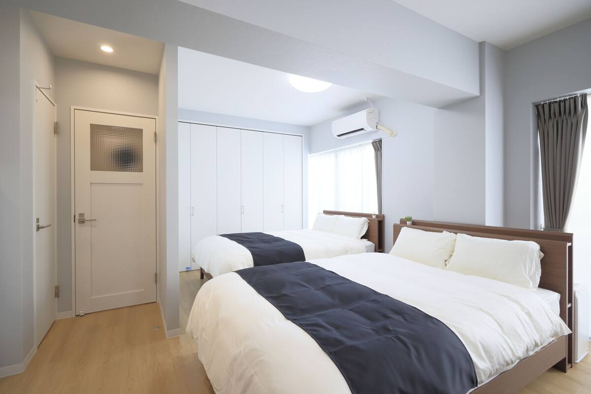 Une chambre d’hôtel avec deux lits, une armoire, un ventilateur de plafond et une fenêtre avec des rideaux.
