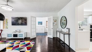 Een modern interieur met een houten vloer, witte muren, een kleurrijk geometrisch vloerkleed en een keuken met een spoelbak en kookplaat.