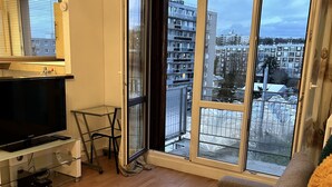 En moderne stue med et stort skydedørsvindue, der fører til en balkon, et fladskærms-tv, et lille bord og en farverig måtte.