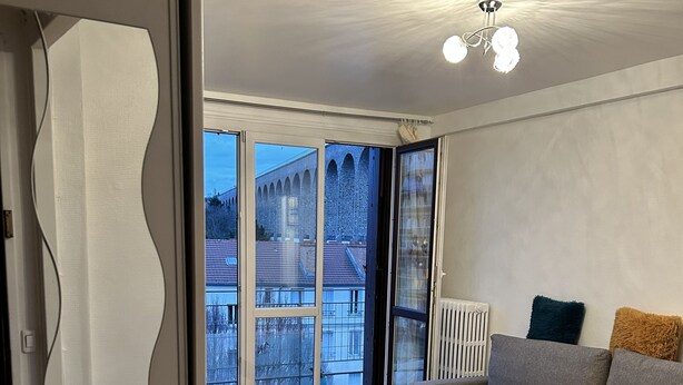 En rummelig stue med et stort vindue, en sofa, et glasbord og en radiator.