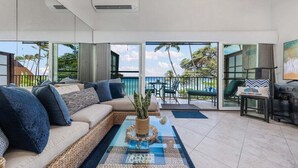 A modern living room with a sofa, a coffee table, and a view of the outdoors. - OceanFront 2BD with Ocean Views and AC - Hoyochi Nikko 208 (Lahaina)