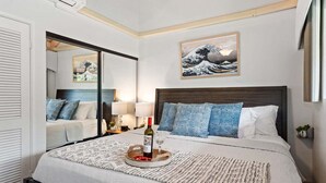 A modern hotel room with a large bed, a bedside table with a lamp, a wall-mounted artwork, and a window with a view. - OceanFront 2BD with Ocean Views and AC - Hoyochi Nikko 208 (Lahaina)