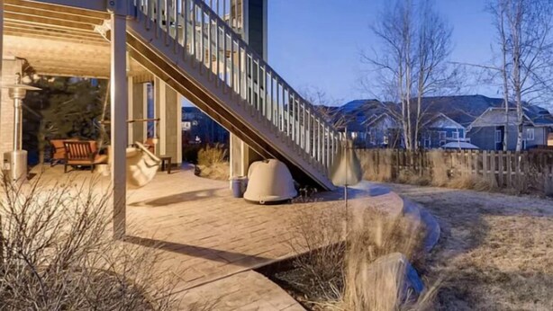 Une terrasse extérieure moderne, dotée d’un escalier menant à un espace abrité, entourée d’un jardin aménagé et avec des immeubles d’habitation en arrière-plan.