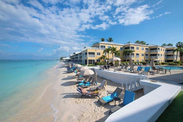 A beach resort with a pool area, sun loungers, and a building with balconies.