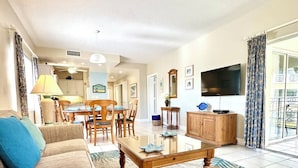 Una sala de estar con sofá, una mesa de centro, televisor y un comedor con sillas y una mesa.