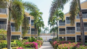 Un hotel de varios pisos, palmeras y un camino bordeado de flores coloridas.