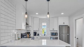 Une cuisine moderne avec des meubles blancs, des appareils en acier inoxydable et un grand îlot central doté de tabourets.