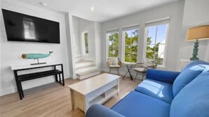 Ein modernes Wohnzimmer mit einem blauen Sofa, einem weißen Couchtisch, einer schwarzen Bank und einem flachbildfernseher an der Wand.