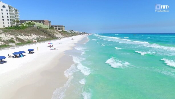 Une plage à l’eau turquoise et limpide, avec un rivage sablonneux et quelques parasols.