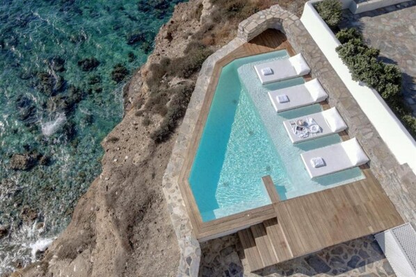 An aerial view of a pool with clear water, surrounded by stone walls and wooden decking. - Iliada Suites Adults Only (Naxos)