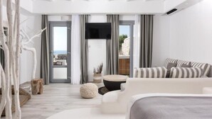 A modern, minimalist living room with a white sofa, a round coffee table, and a flat-screen TV mounted on the wall. - Iliada Suites Adults Only (Naxos)