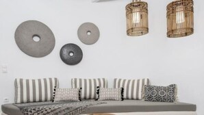 A modern living room with a grey sofa, striped cushions, a woven pouf, and a round pouf. - Iliada Suites Adults Only (Naxos)