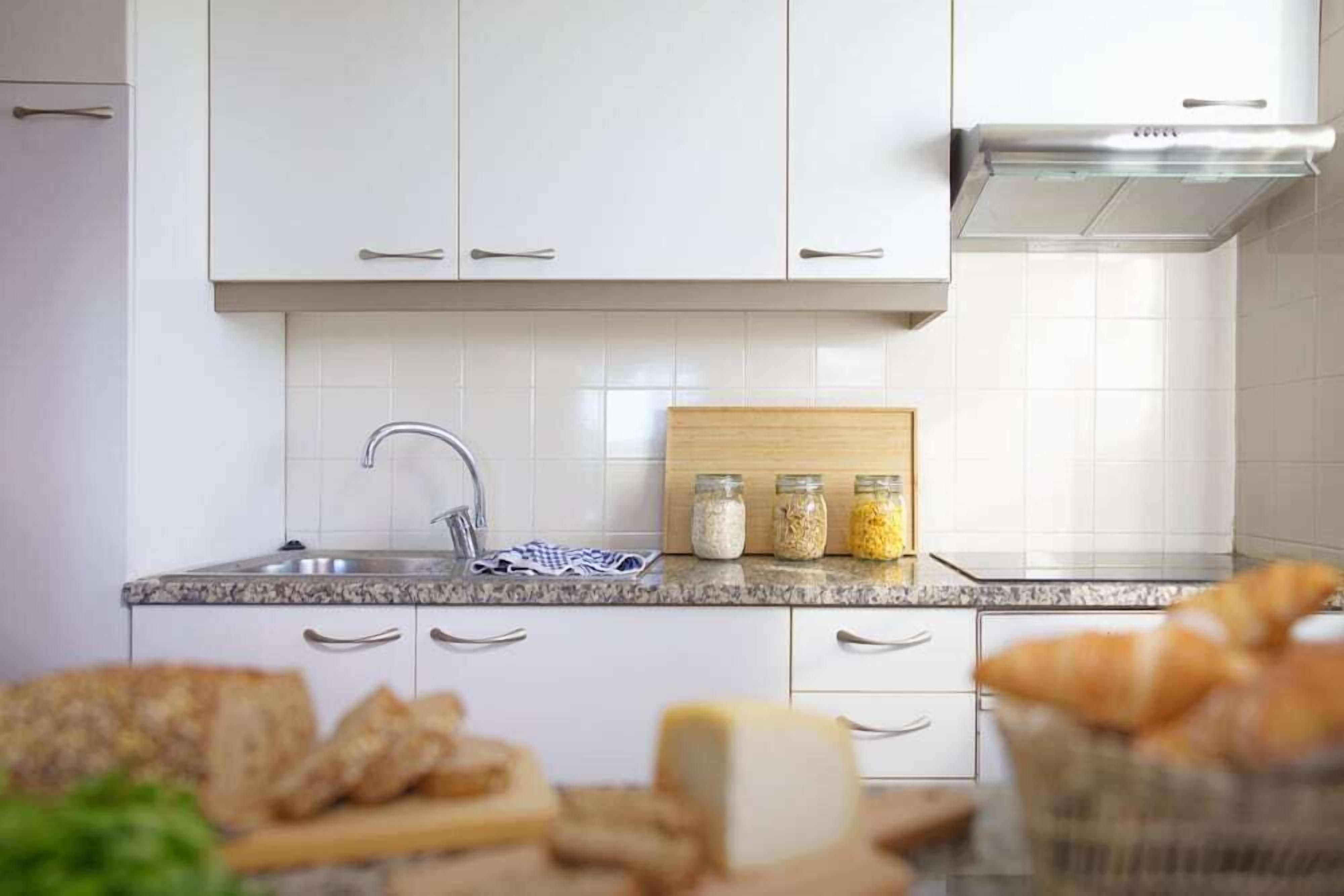 Une cuisine avec des meubles blancs, un plan de travail en granit, un évier en acier inoxydable et une planche à découper en bois.