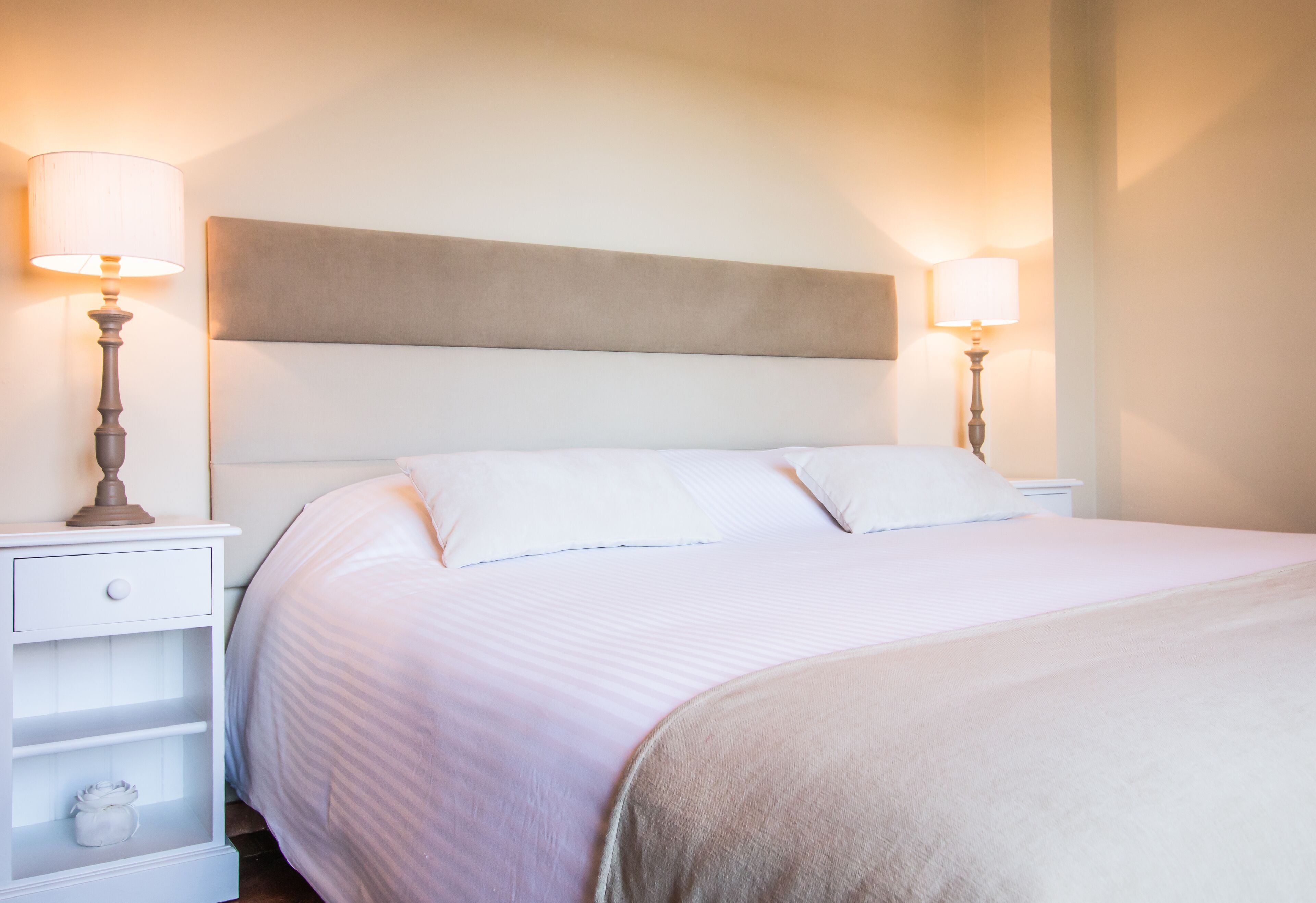 A neatly made bed with white linens and a beige headboard in a hotel room.