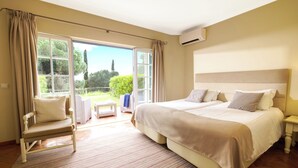 Un dormitorio con una cama grande, una silla, una mesita y vistas al exterior a través de una puerta corredera.