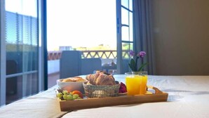 Bandeja de desayuno con cruasanes, uvas y jugo de naranja sobre una cama con vista a un balcón.