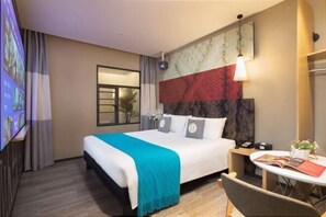 A hotel room with a bed, bedside table, and a small table with a chair.