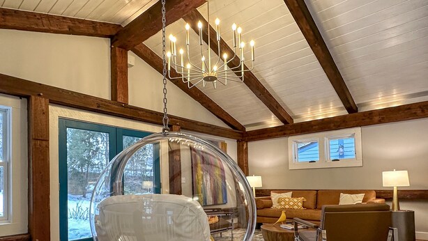 Ein großzügiges Wohnzimmer mit Hängesessel, Holzbalken, einer Chandelier und einem großen Fenster.