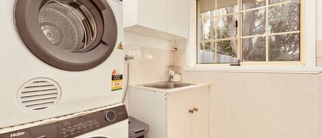 A laundry room with a front-loading washer and dryer, a sink, and a window with a view of trees.