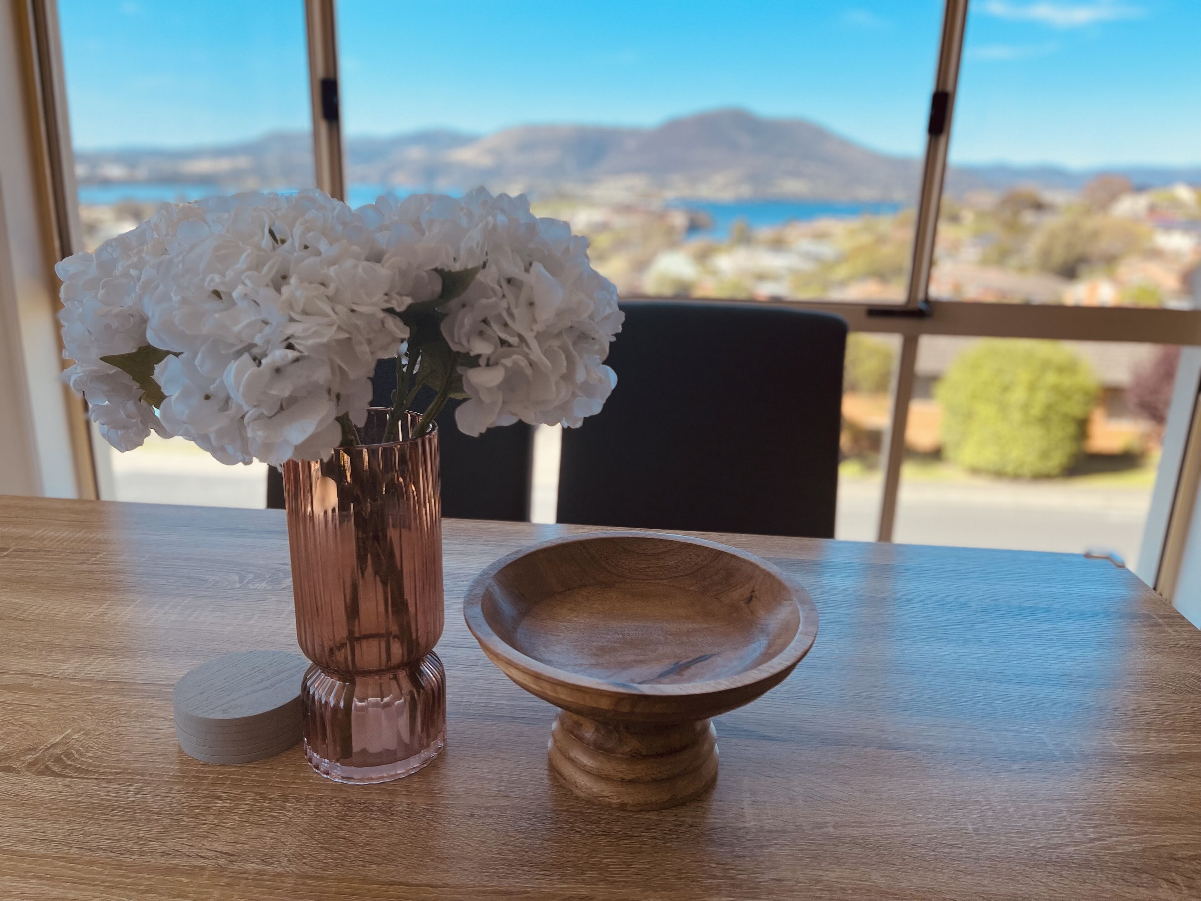 Une table sur laquelle se trouve un vase rempli de fleurs blanches et un bol en bois.