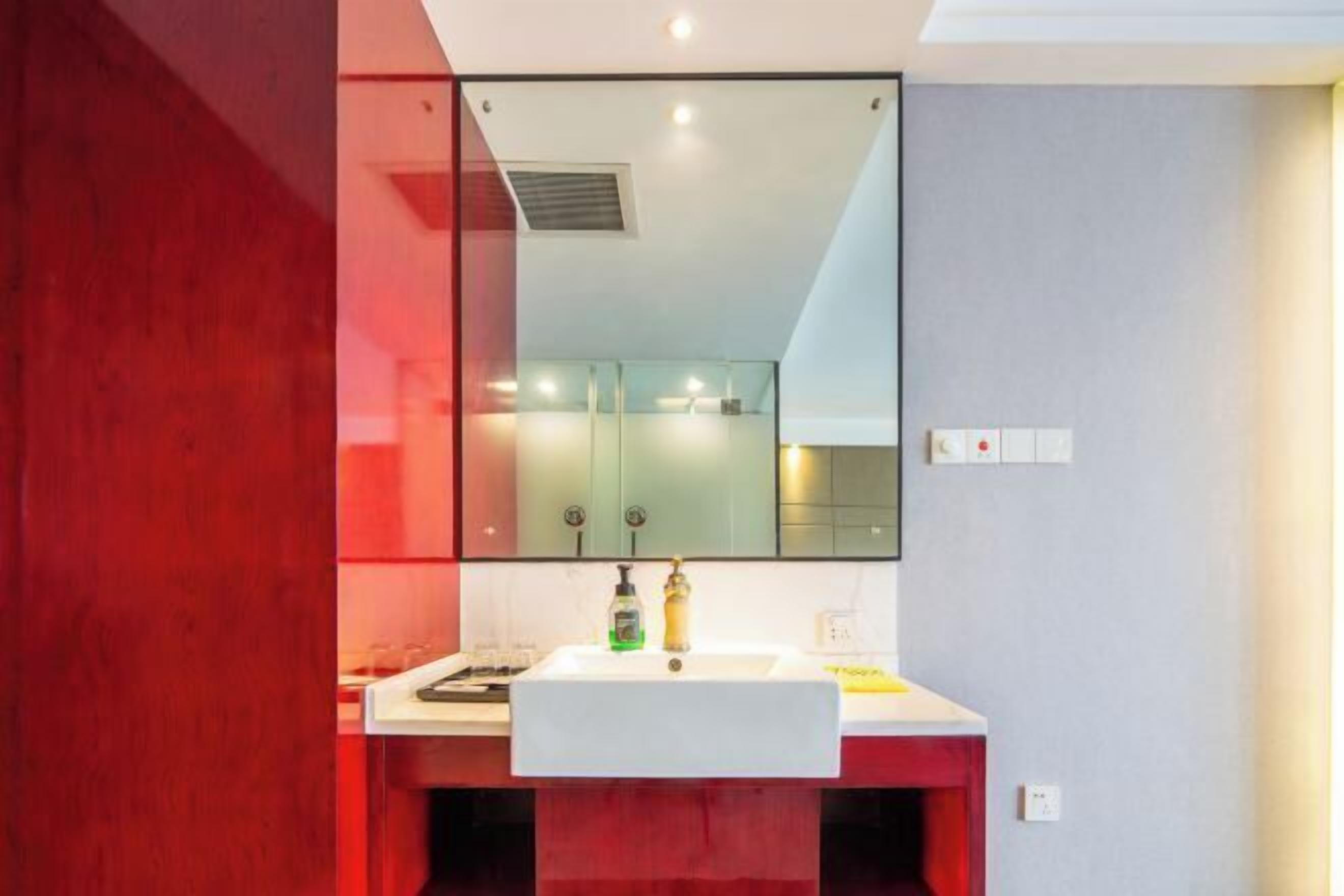 A modern bathroom with a white sink, red cabinetry, and a large mirror above the sink.