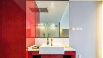 A modern bathroom with a white sink, red cabinetry, and a large mirror above the sink.
