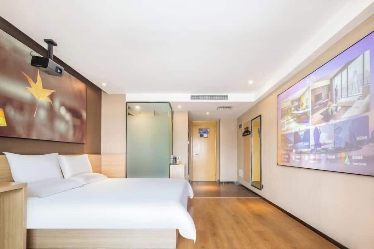 A hotel room with a bed, a projector screen, and a wall-mounted camera.