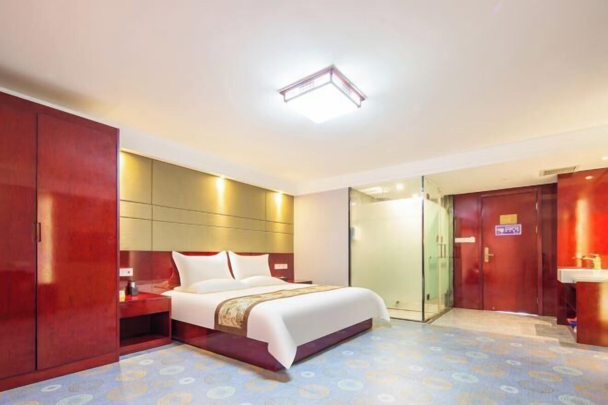 A hotel room with a bed, bedside table, wardrobe, and a bathroom visible through a glass door.