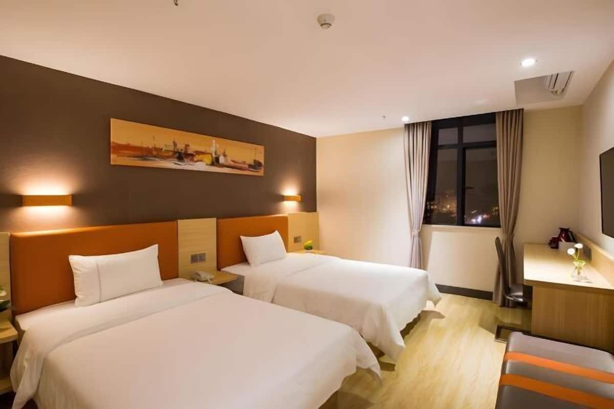 A hotel room with two beds, a desk, a chair, and a painting on the wall.