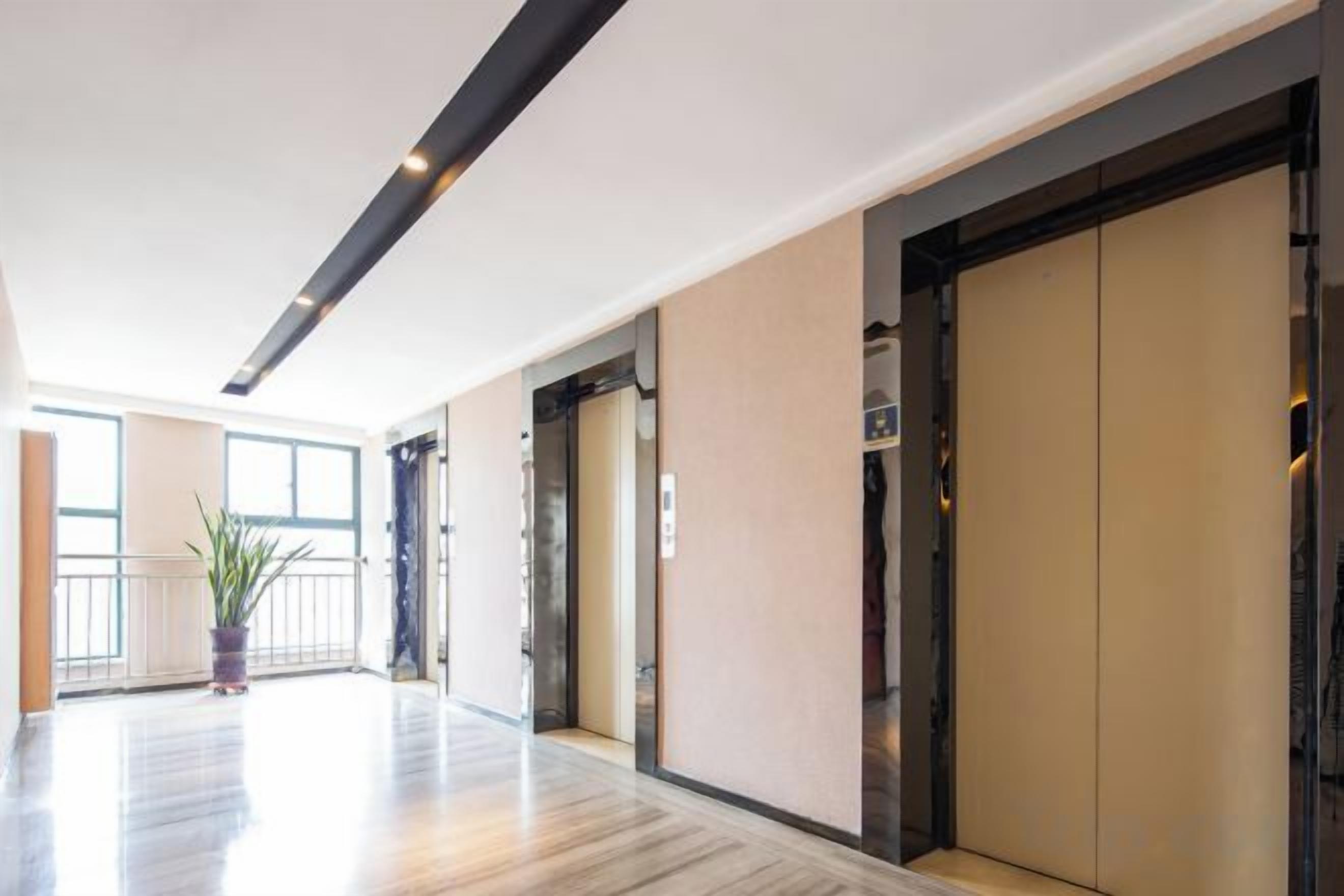 A modern hotel lobby with a wooden floor, a potted plant, and a large elevator.