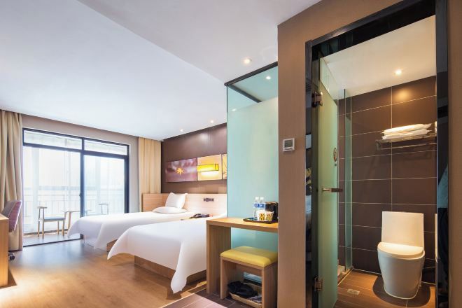 A hotel room with two beds, a sitting area, a bathroom with a modern toilet, and a large window providing natural light.