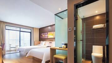 A hotel room with two beds, a sitting area, a bathroom with a modern toilet, and a large window providing natural light.