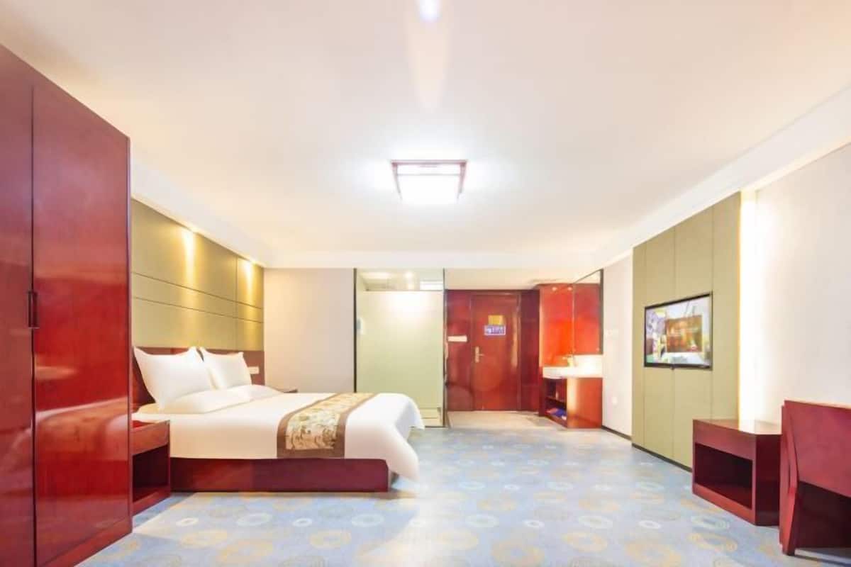 A hotel room with a bed, wardrobe, and a bathroom with a sink and mirror.
