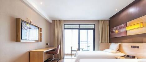 Habitación de hotel con cama, escritorio, silla, televisión y un ventanal grande.