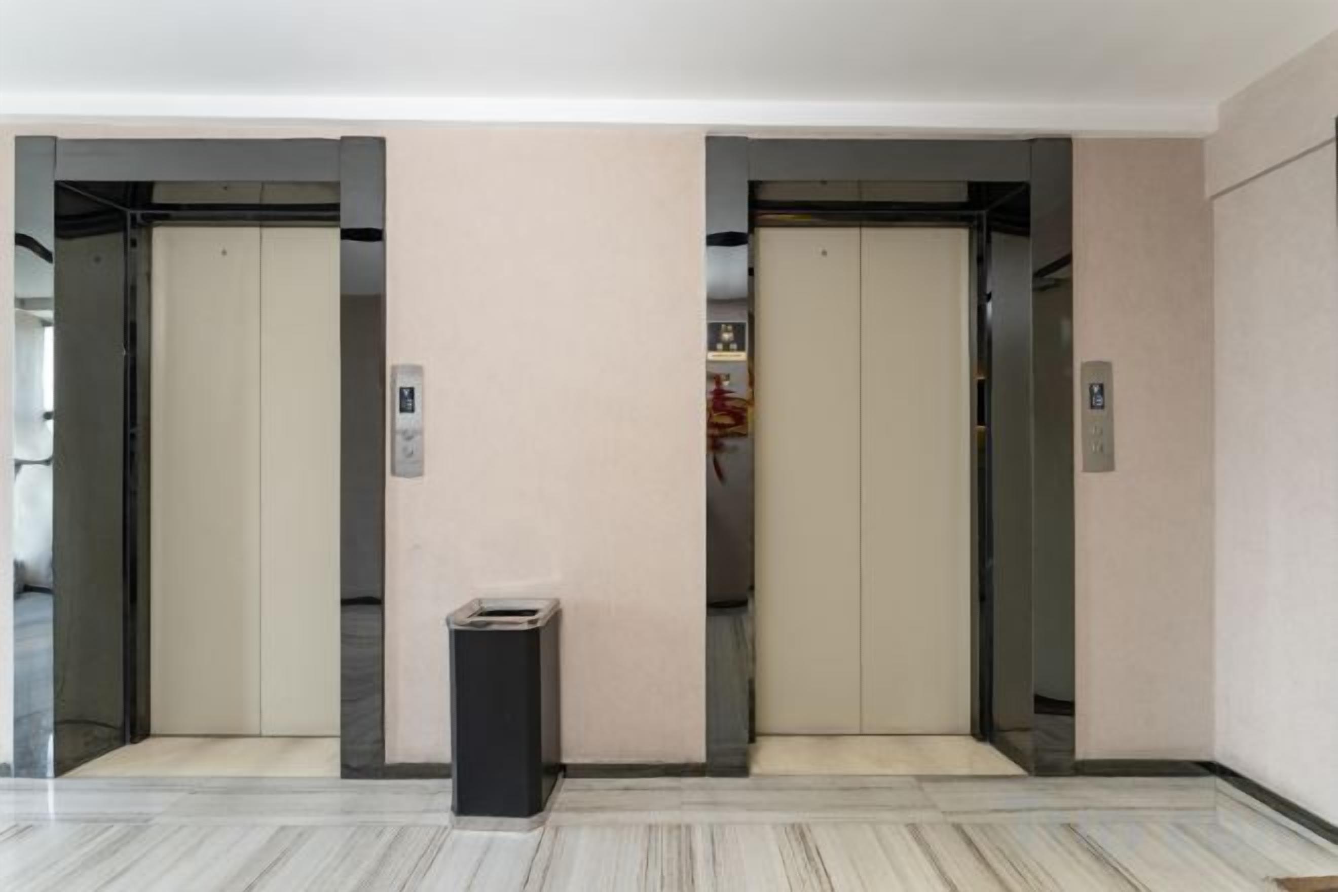 An elevator area with two elevators, a trash bin, and a wall-mounted emergency phone.