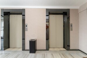 An elevator area with two elevators, a trash bin, and a wall-mounted emergency phone. - IU Hotel (Yanshi Baima Temple) (Luoyang)