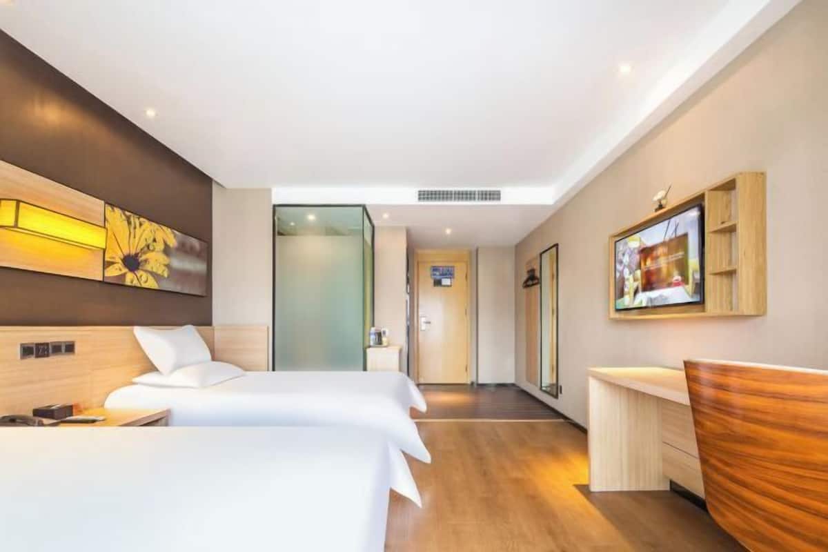 A hotel room with two beds, a desk, a TV, and a large window.
