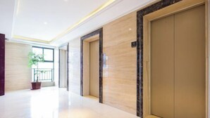 A hallway with a potted plant, a marble wall, and a door with a black frame. - IU Hotel (Yanshi Baima Temple) (Luoyang)